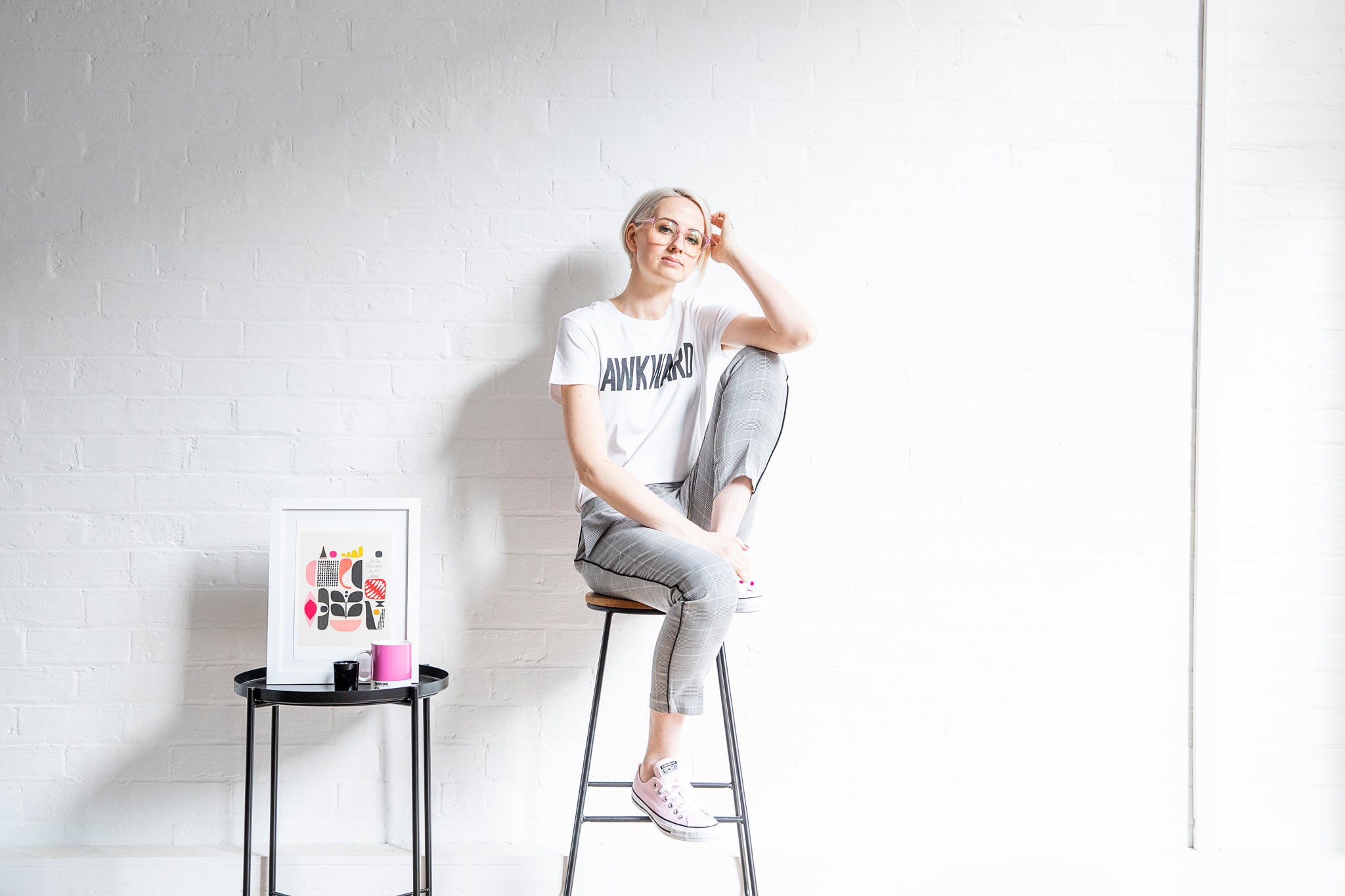 Woman with blonde hair and glasses on a stool wearing slogan tee that says Awkward