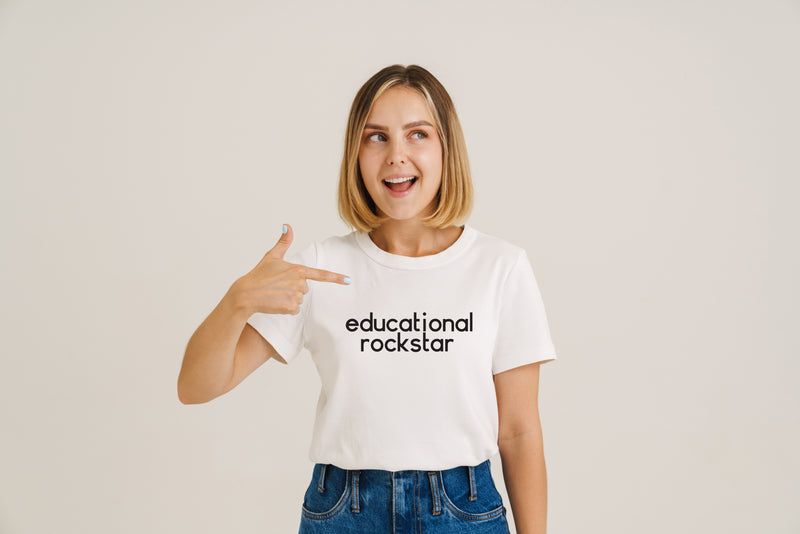 Women wit blonde bob style hair cut pointing at the slogan on her white tshirt that says educational rockstar
